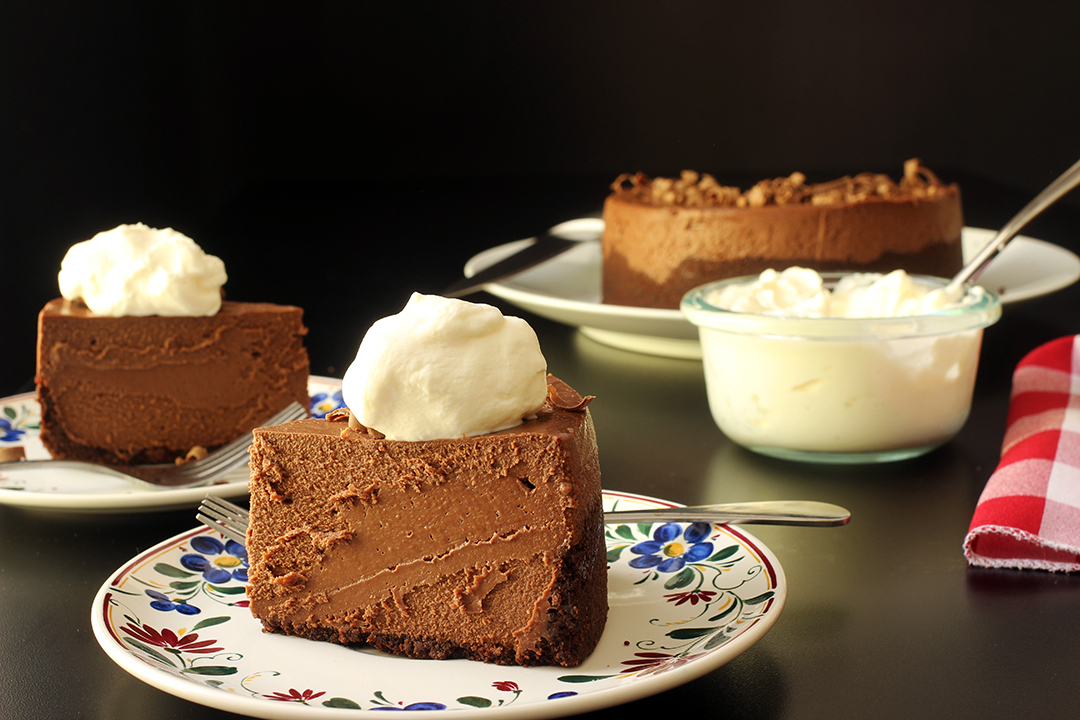 slices of chocolate cheesecake on plates on table with whipped cream and napkins.