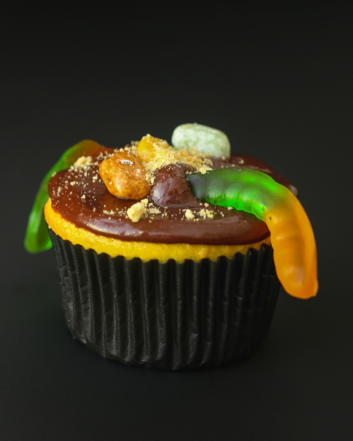 close up of a cupcake with mud frosting and a gummy worm.