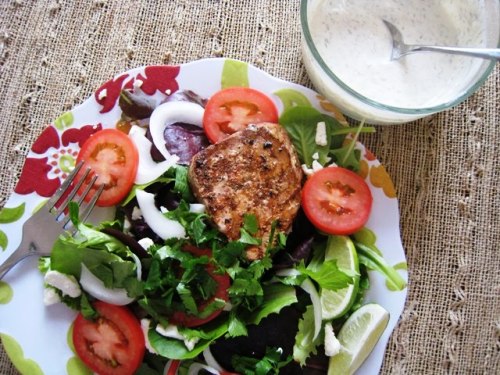 A plate of salad with fish and creamy dressing on a table.