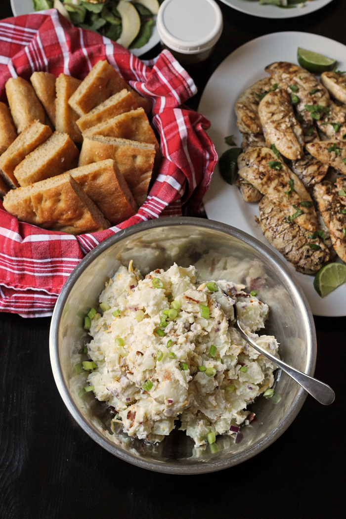 dinner spread of potato salad, bread basket and grilled chicken