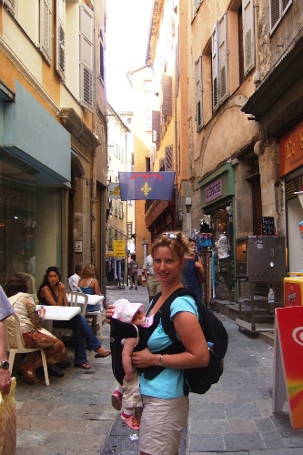 A woman walking down a city street with a baby in a front pack.