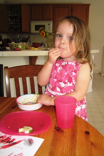 A little girl licking hummus off her hand