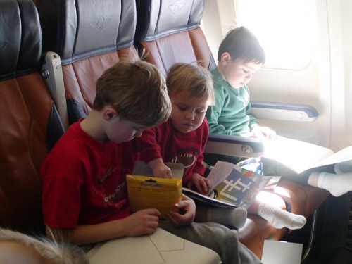 Three boys in airplane seats working on projects.