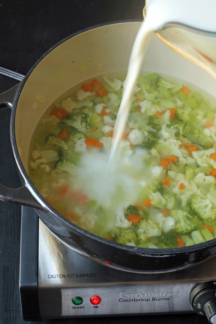 pouring milk into broccoli cauliflower soup