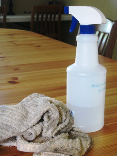 Spray bottle and cleaning rag on a wooden table.