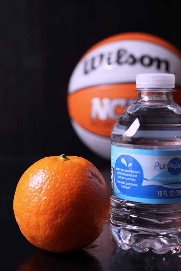 A close up of a water bottle and an orange in front of a basketball.