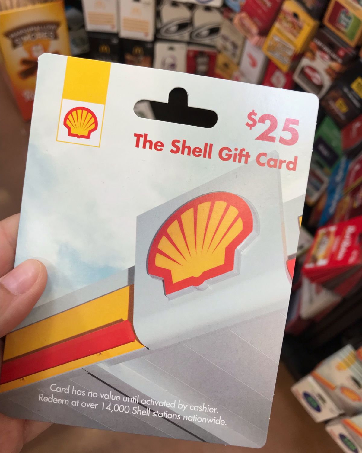 hand holding shell gift card in front of gift card display.