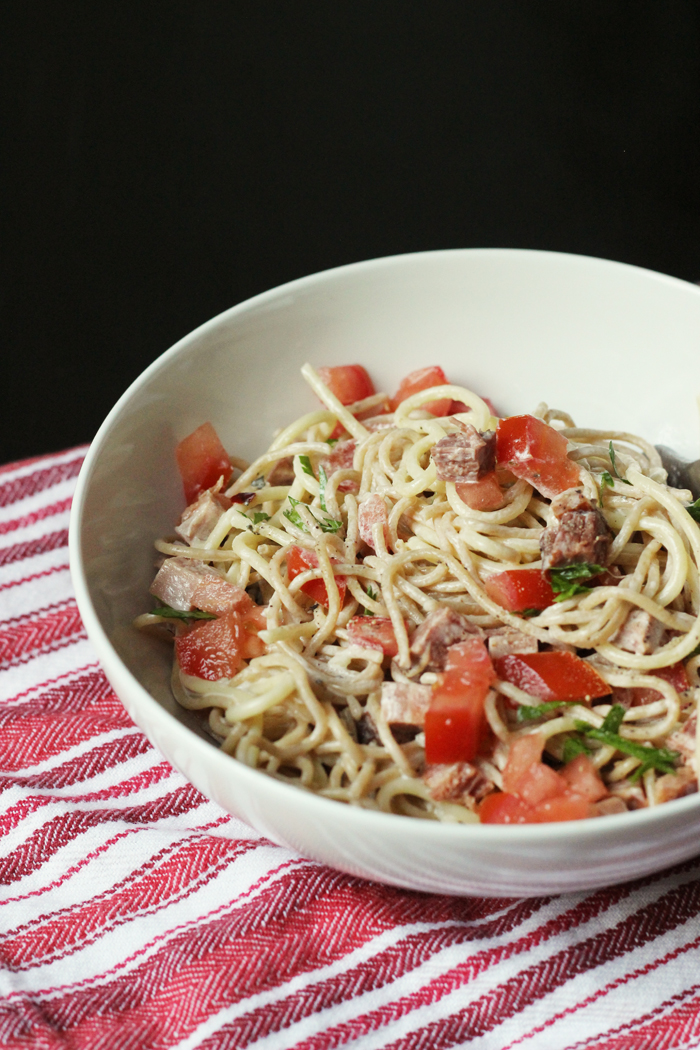 A bowl of creamy noodles and ham, with tomatoes