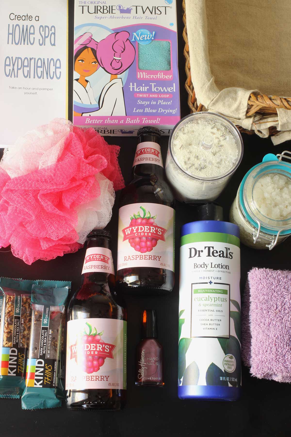 spa gift basket fillers laid out in an array on a black table top.