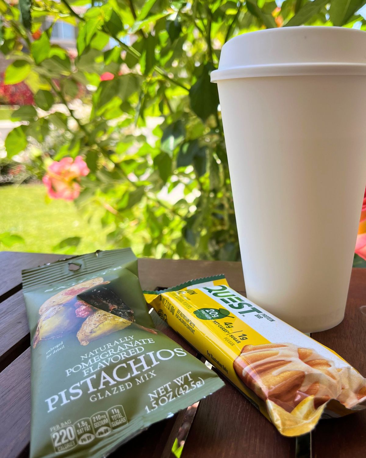 to go coffee cup on a table with breakfast snacks, in front of a rose bush.