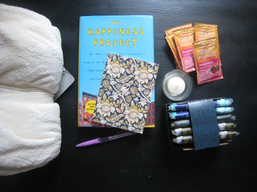 Blanket, tissue, journal, pen, candle, book, and vitamin C on table.