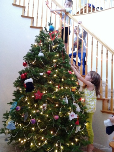 A girl hanging an ornament on a christmas tree near a stairwell.