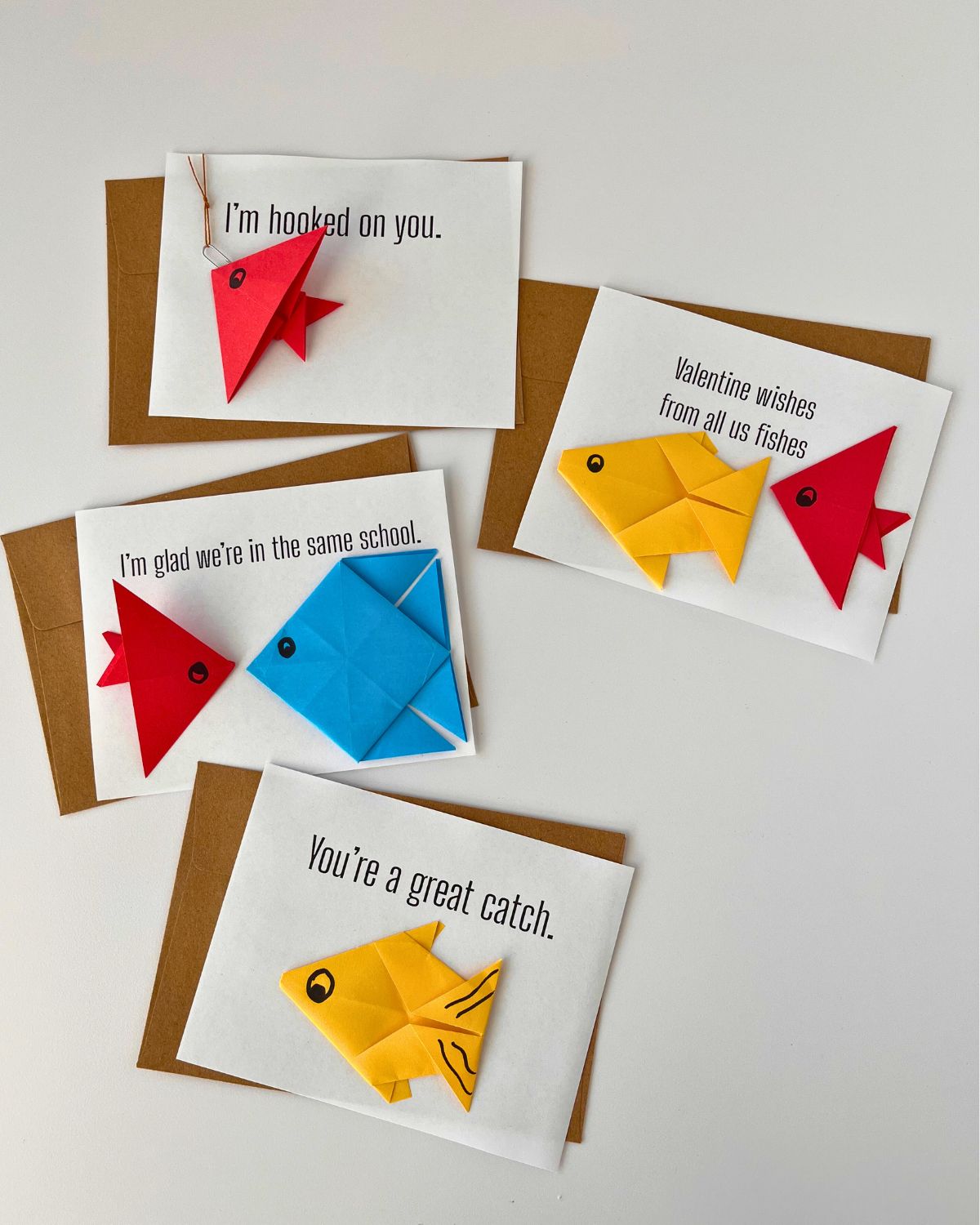 array of four origami fish valentine cards with brown envelopes on a white background.
