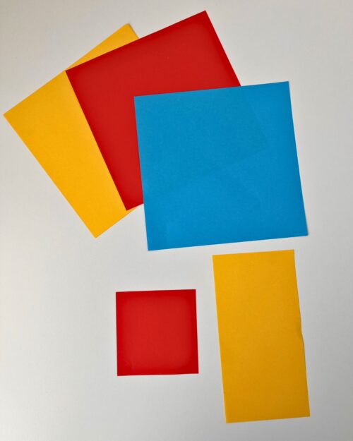 yellow, red, and blue origami paper in different sizes on white surface.