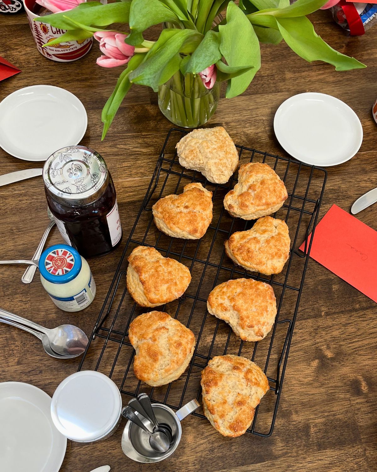 valentine scones on cooling rack with jam and cream on table nearby.