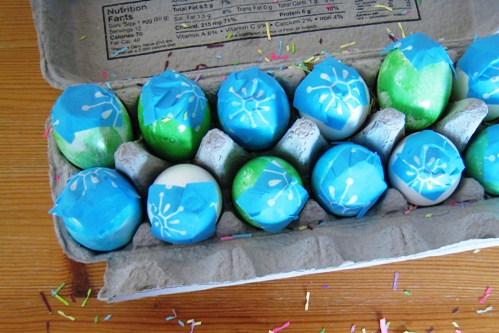 A dozen confetti eggs in carton with confetti on table.