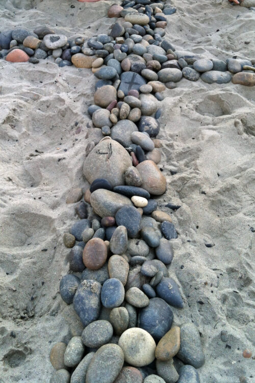 Rocks piled to represent a cross in the sand.
