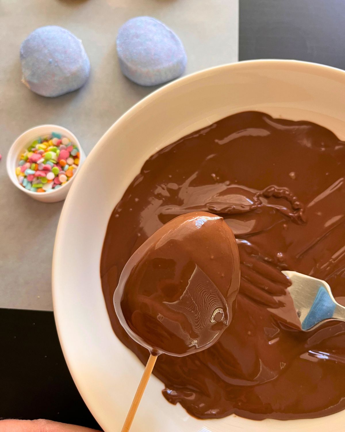 dipped marshmallow egg above melted chocolate bowl.