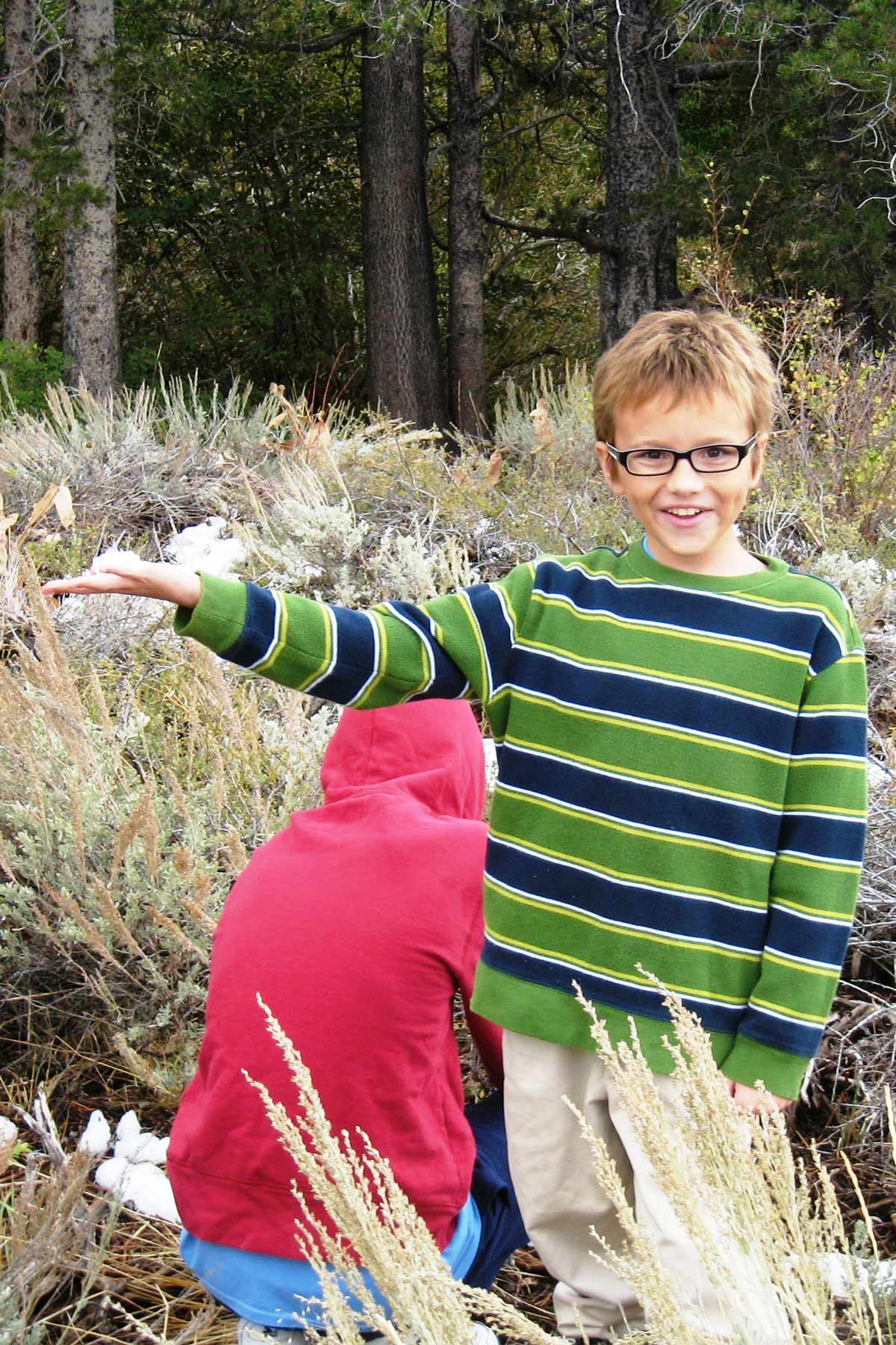 boy in striped sweater in nature with arm outstretched.