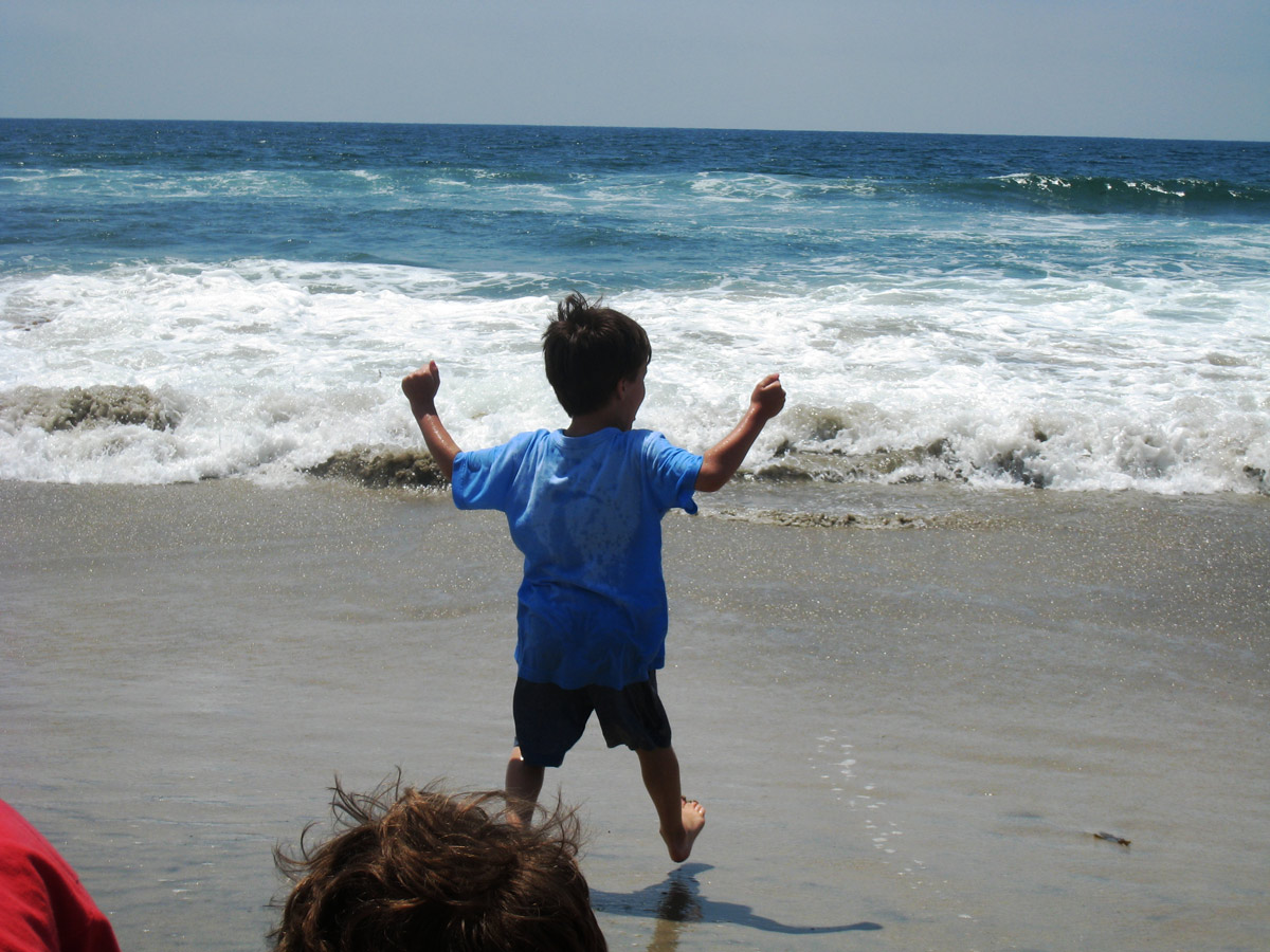 boy with raised arms waiting for a wave to approach on beach.