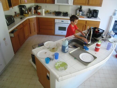 A boy in a kitchen doing dishes.