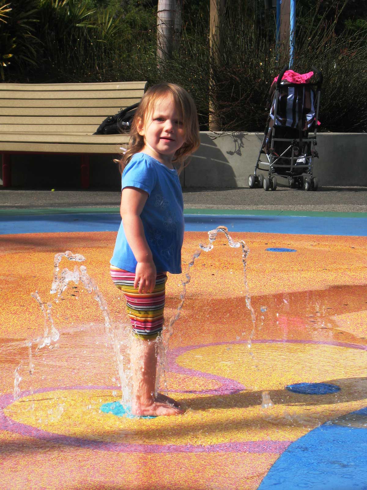 little girl in pastel clothes standing on a pastel splashpad.