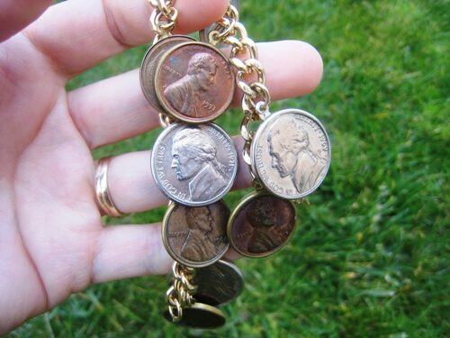 Holding bracelet of coins in hand over grass.
