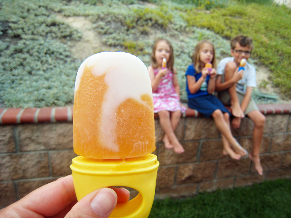 hand holds popsicle, with kids eating on wall