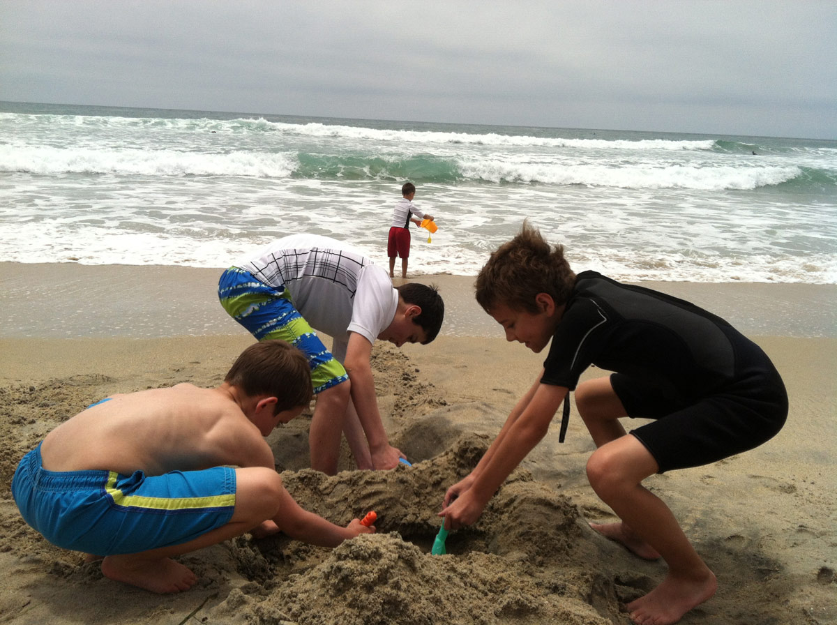 group of boys digging into sand at beach.
