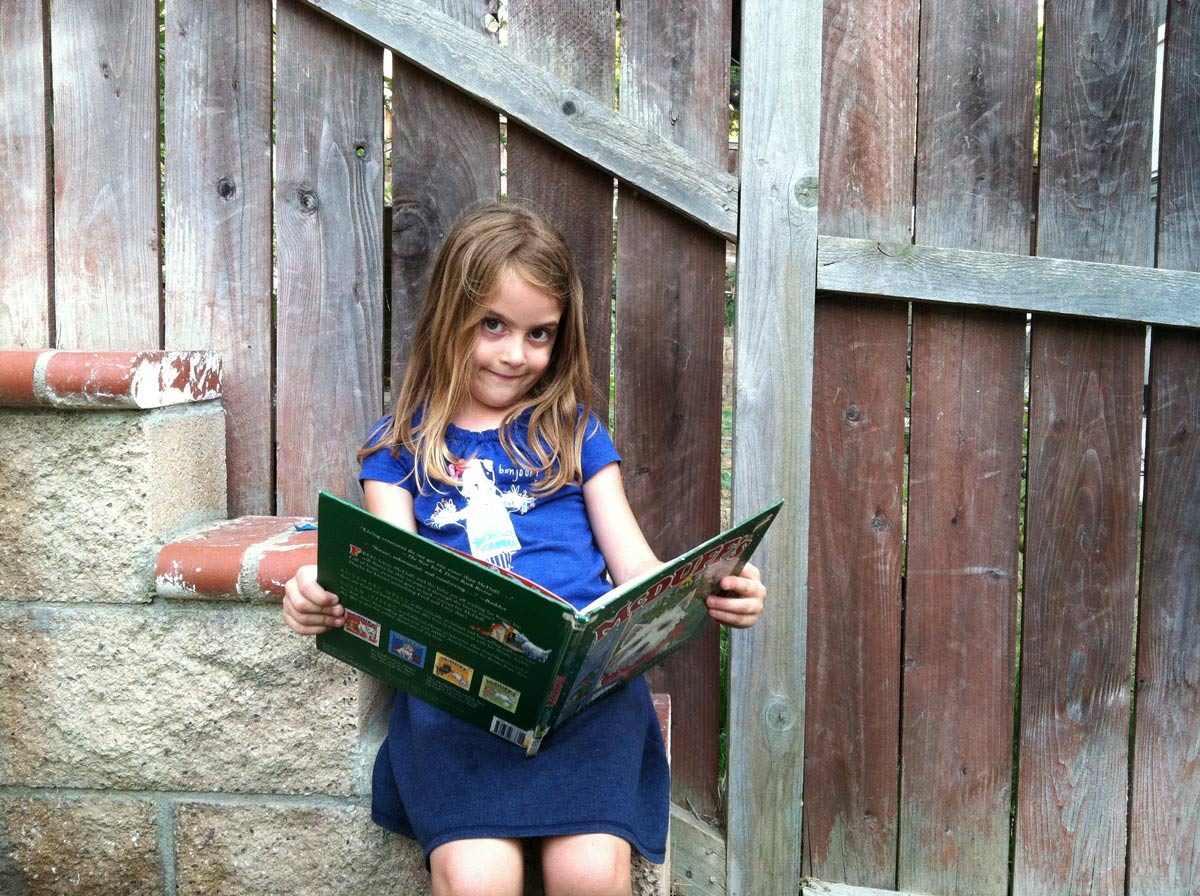 girl leaning against garden wall holding a picture book.