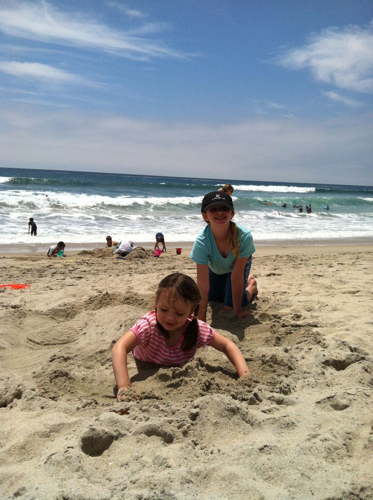 girls burying each other in sand at the beach.