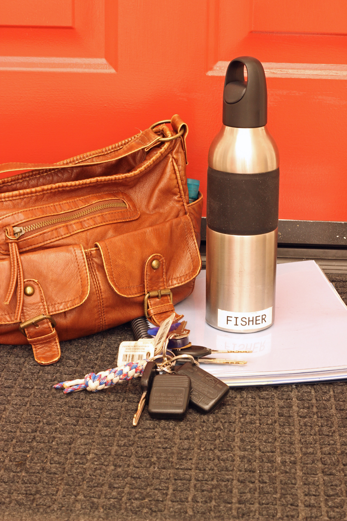 A purse, keys, water bottle, and planner sitting by the front door.