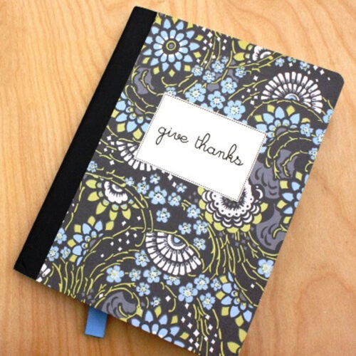 overhead shot of composition book covered in pretty scrapbook paper with a ribbon bookmark and a label that reads give thanks.