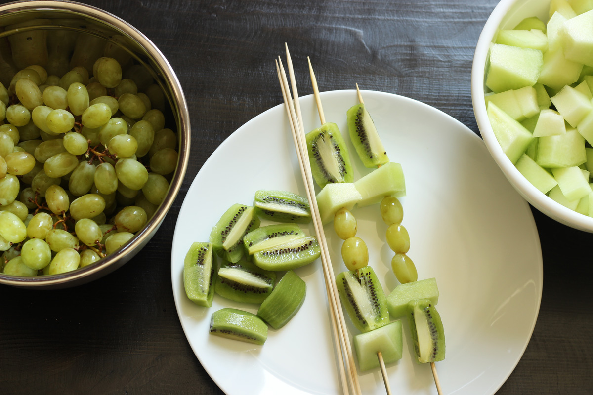 platter of green fruit kabobs with bowls of fruit