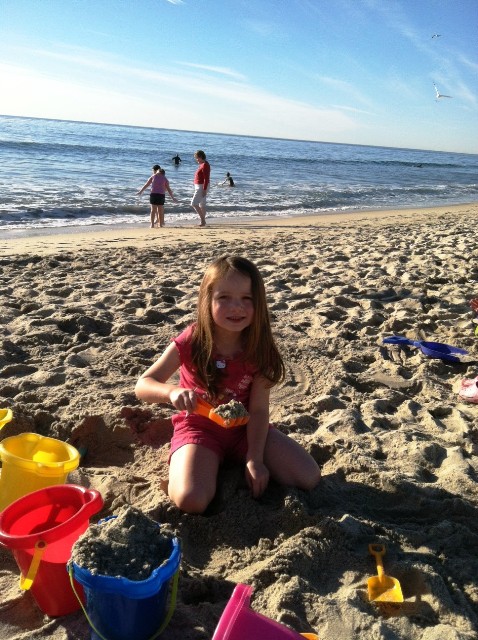 A girl sitting at a beach, building a sand castle.