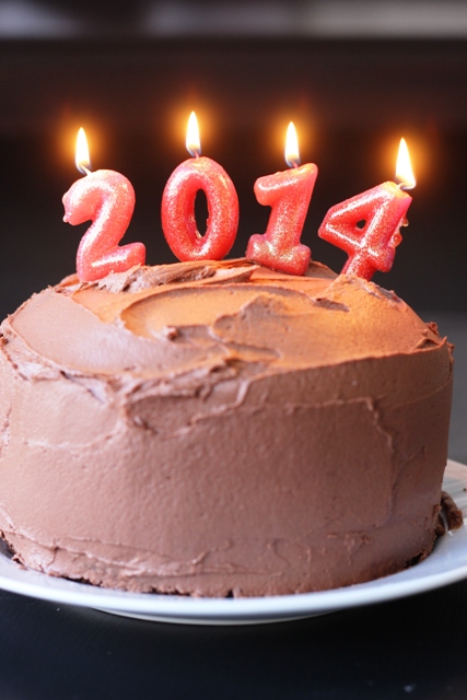 A chocolate birthday cake with lit candles for 2014.