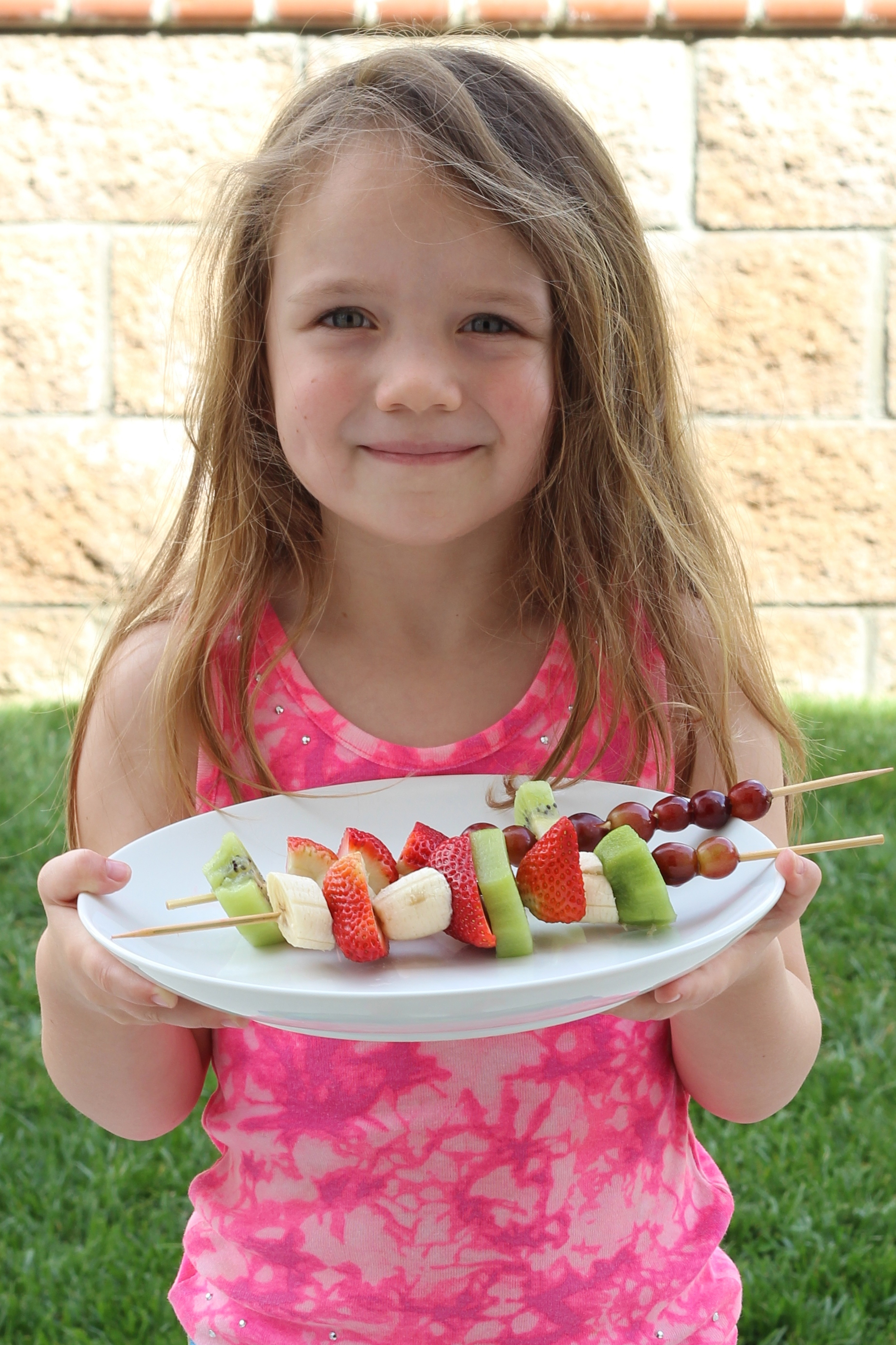 A little girl holding a platter of fruit skewers