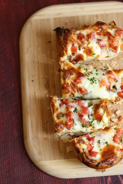 French bread pizza sitting on top of a wooden cutting board