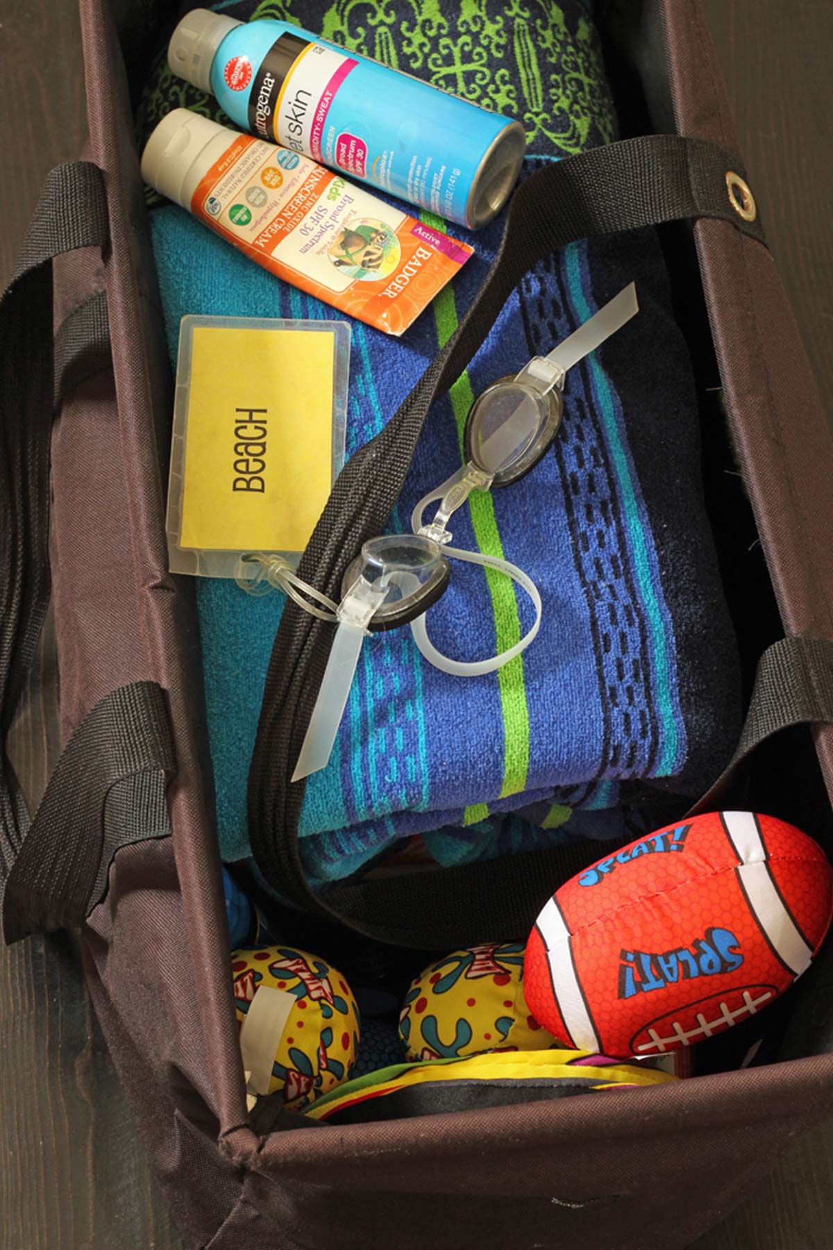 black beach bag packed with towels, sunscreen, and toys.