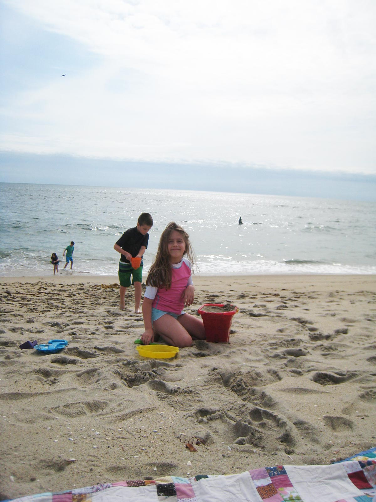 girl filling a bucket with sand to build a sand castle.