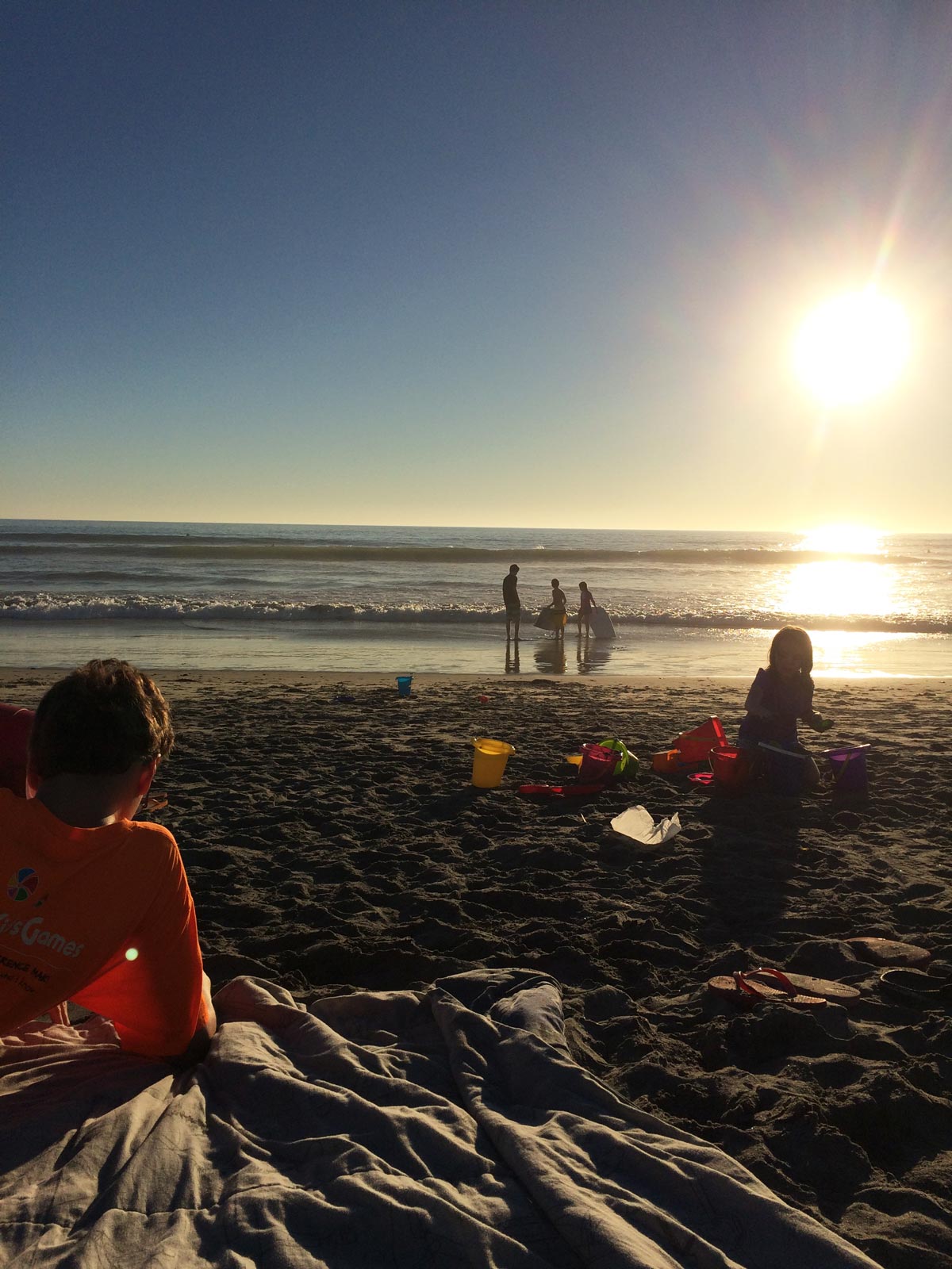 boy lying on beach blanket while kids play on beach at dusk.