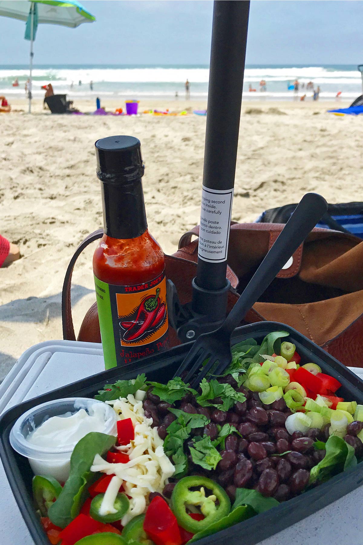 taco salad in meal prep box on cooler under umbrella at the beach.
