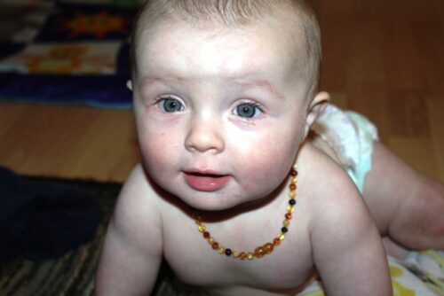 A baby with a teething necklace, looking at the camera.