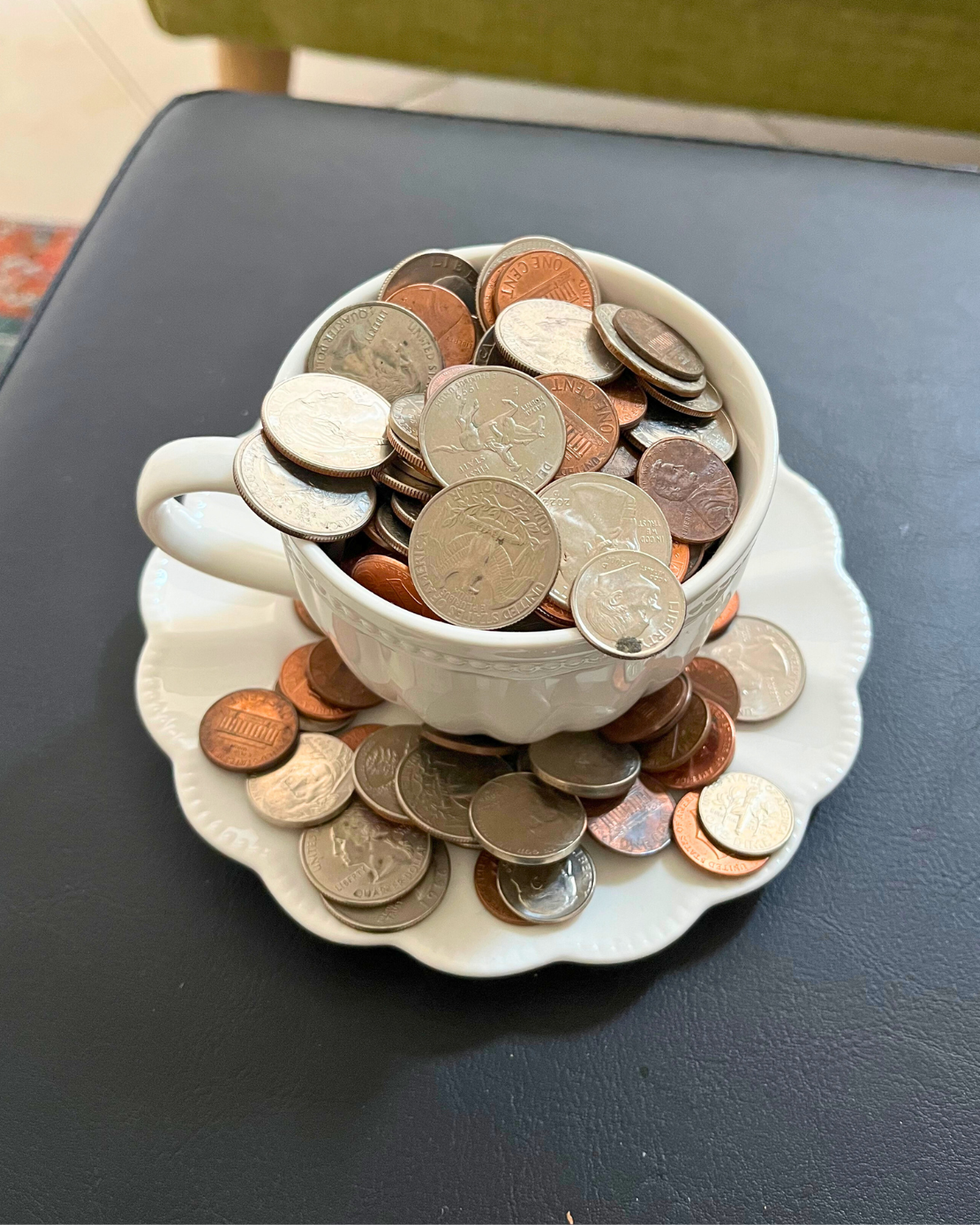 tea cup and saucer overflowing with American coins on leather surface.