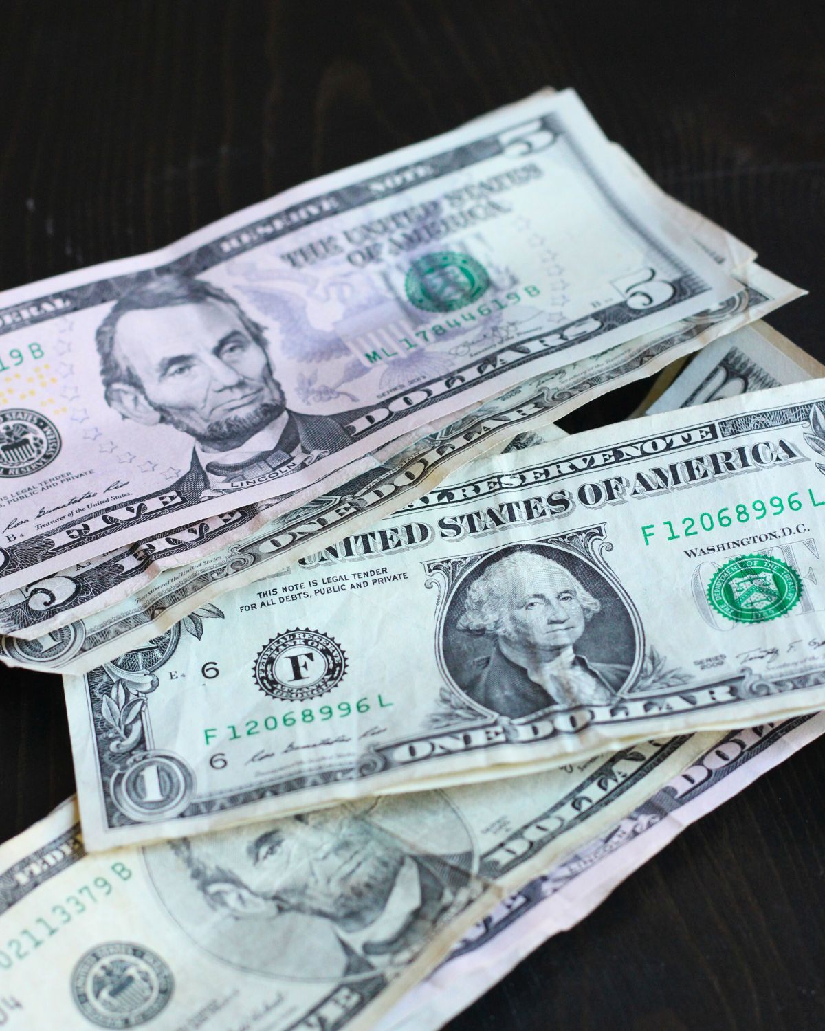stack of five- and one-dollar bills on black surface.