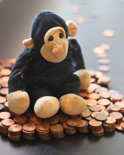 stuffed monkey doll sitting on stacks of pennies on a black table.