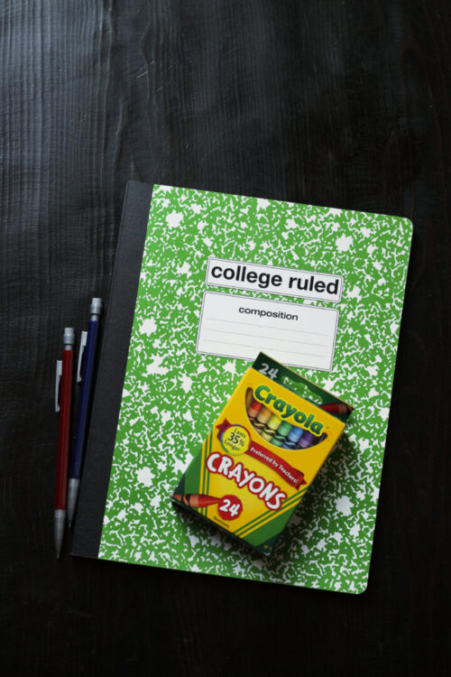 green composition book with a box of crayons and pencils