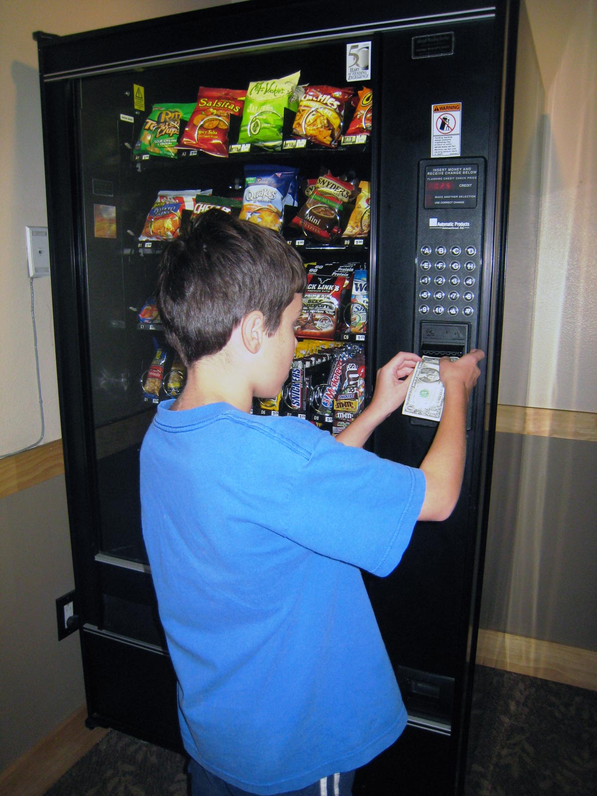 boy inserting dollar bill into vending machine inside hotel or motel.