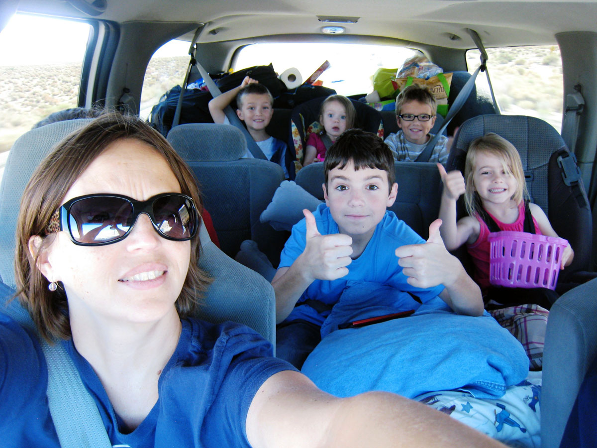 mom in front seat of car with kids giving thumbs up from back seats.