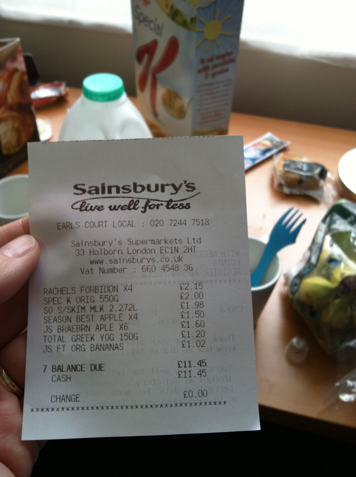 hand holding grocery receipt from uk store with breakfast items in background.